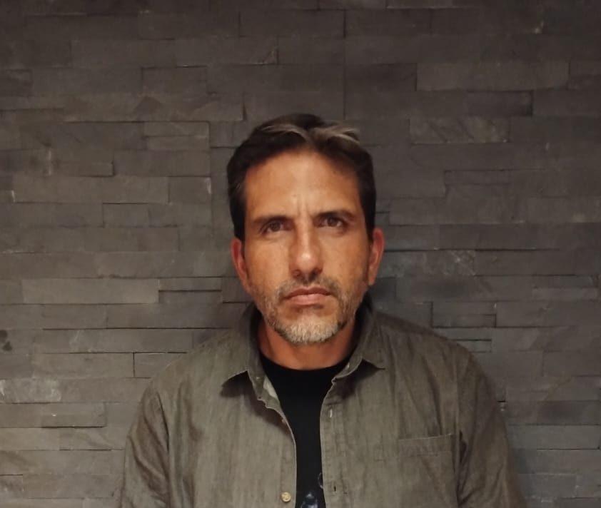 Cristián Brito Villalobos, hombre de mediana edad con barba, vistiendo camisa gris sobre fondo de ladrillo