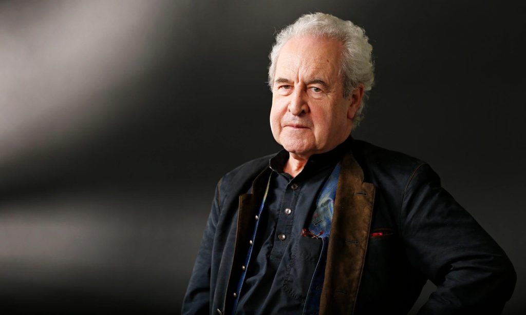 John Banville, escritor irlandés, retratado en primer plano con cabello blanco, expresión seria, vistiendo chaqueta