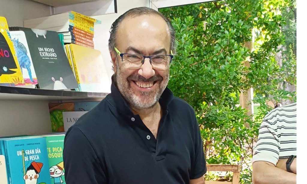 Jesús Marchamalo sonríe ante estantería con libros y plantas verdes de fondo en interior
