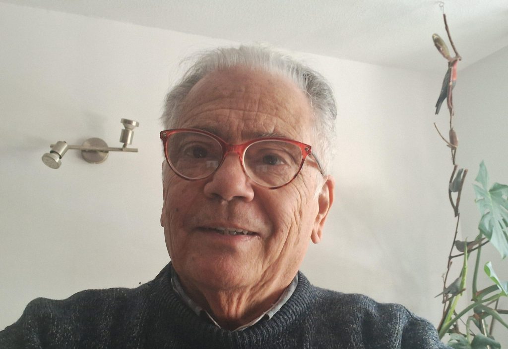 Edmundo Moure Rojas, hombre mayor con gafas, suéter oscuro, mirando a la cámara en interior