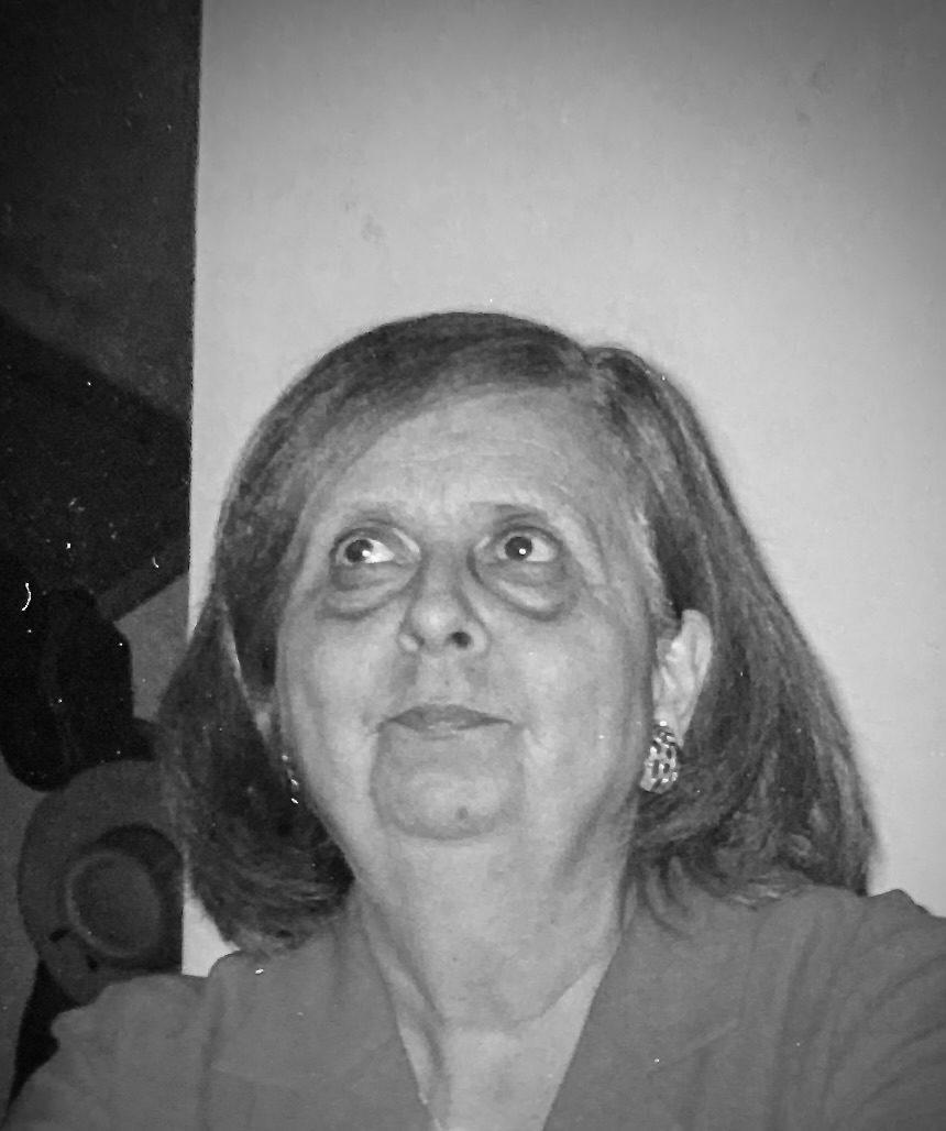 Mujer de mediana edad con cabello largo, gafas, pendientes y expresión pensativa mirando hacia arriba