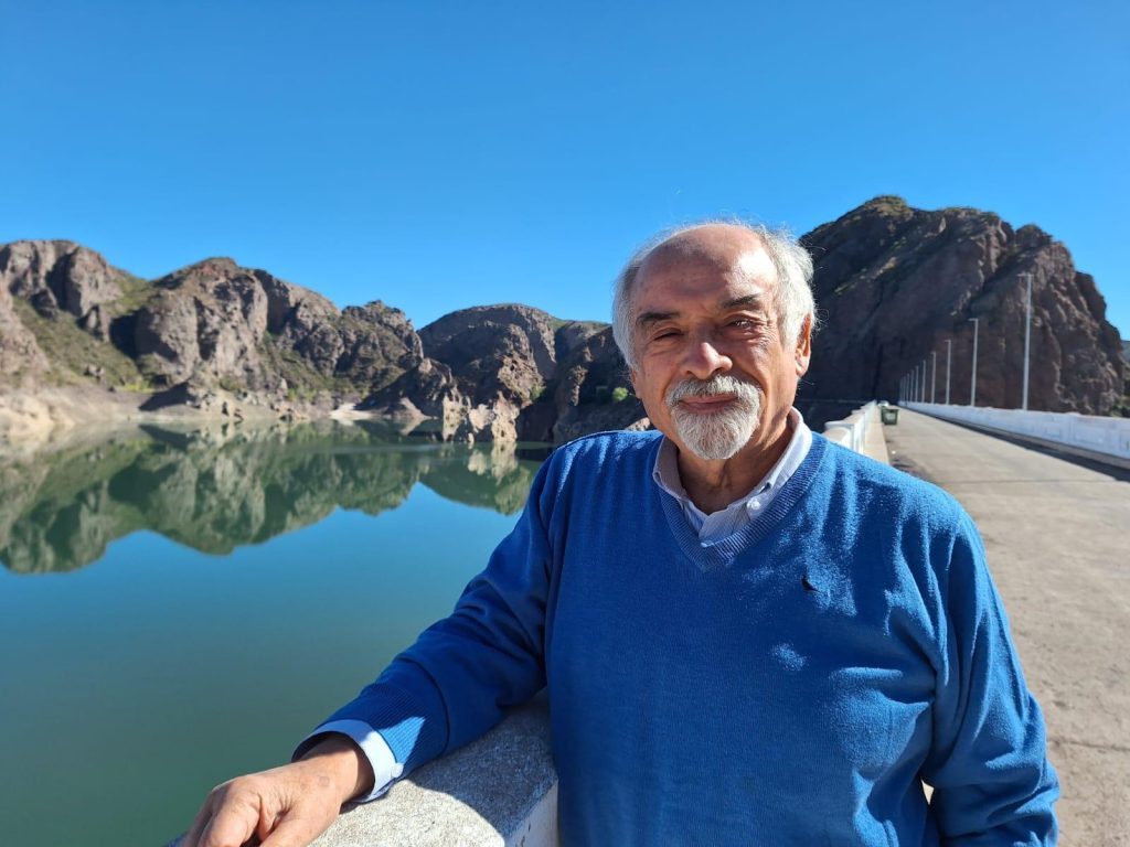 Juan Mihovilovich junto a un lago de aguas turquesas rodeado de montañas rocosas, en ambiente natural