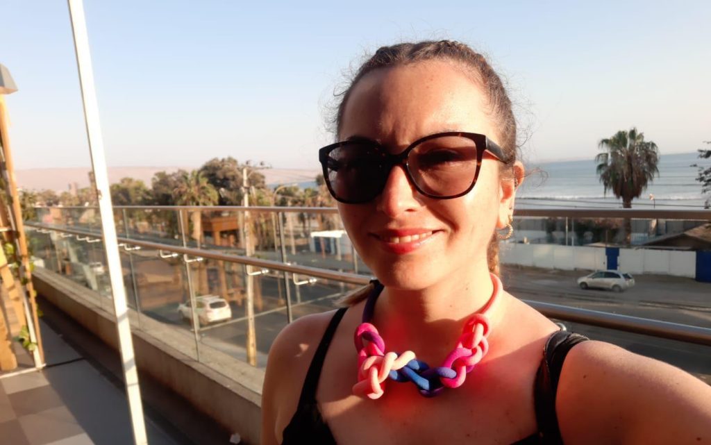 Mujer de gafas de sol y moño rosa sonríe ante paisaje urbano con edificios y montañas al fondo