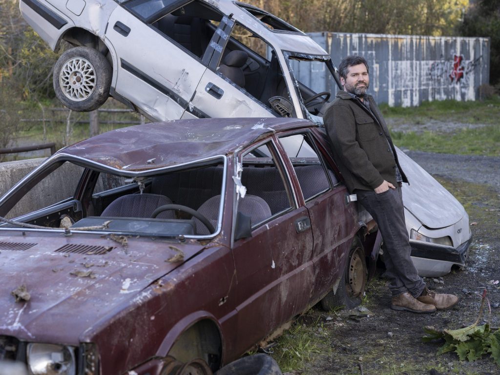Hombre junto a automóviles desmantelados en patio abandonado, escena de desolación urbana