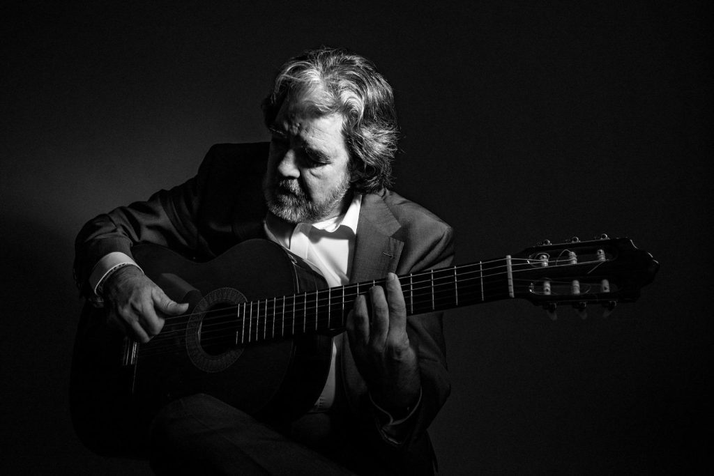 Rafael Riqueni sostiene una guitarra acústica, retrato en blanco y negro con iluminación dramática