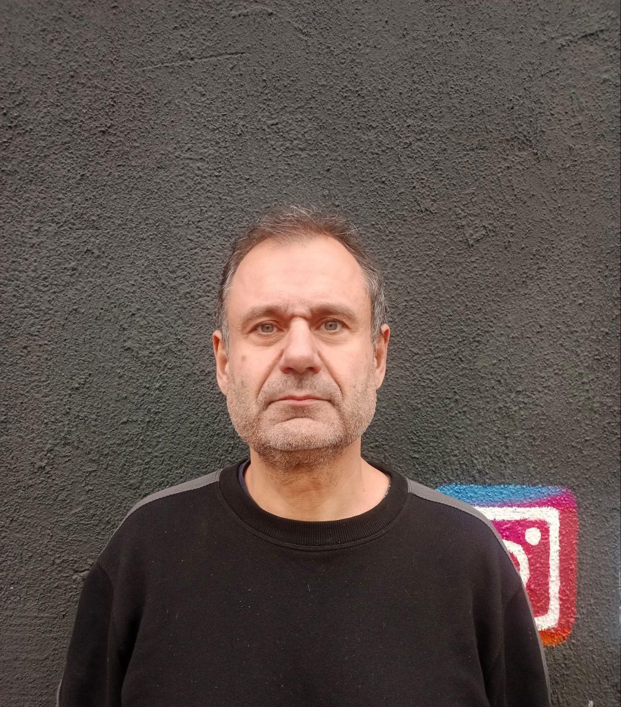 Aníbal Ricci Anduaga, hombre de mediana edad frente a pared gris, viste camiseta negra con detalle de neón