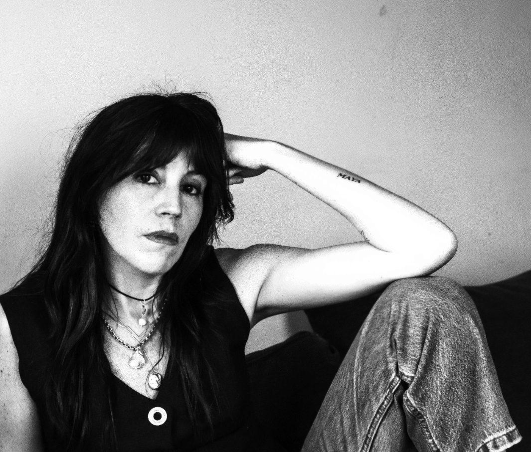 María Paz Rodríguez, retrato en blanco y negro, mujer de cabello largo oscuro con flequillo, collares y mano en cabeza