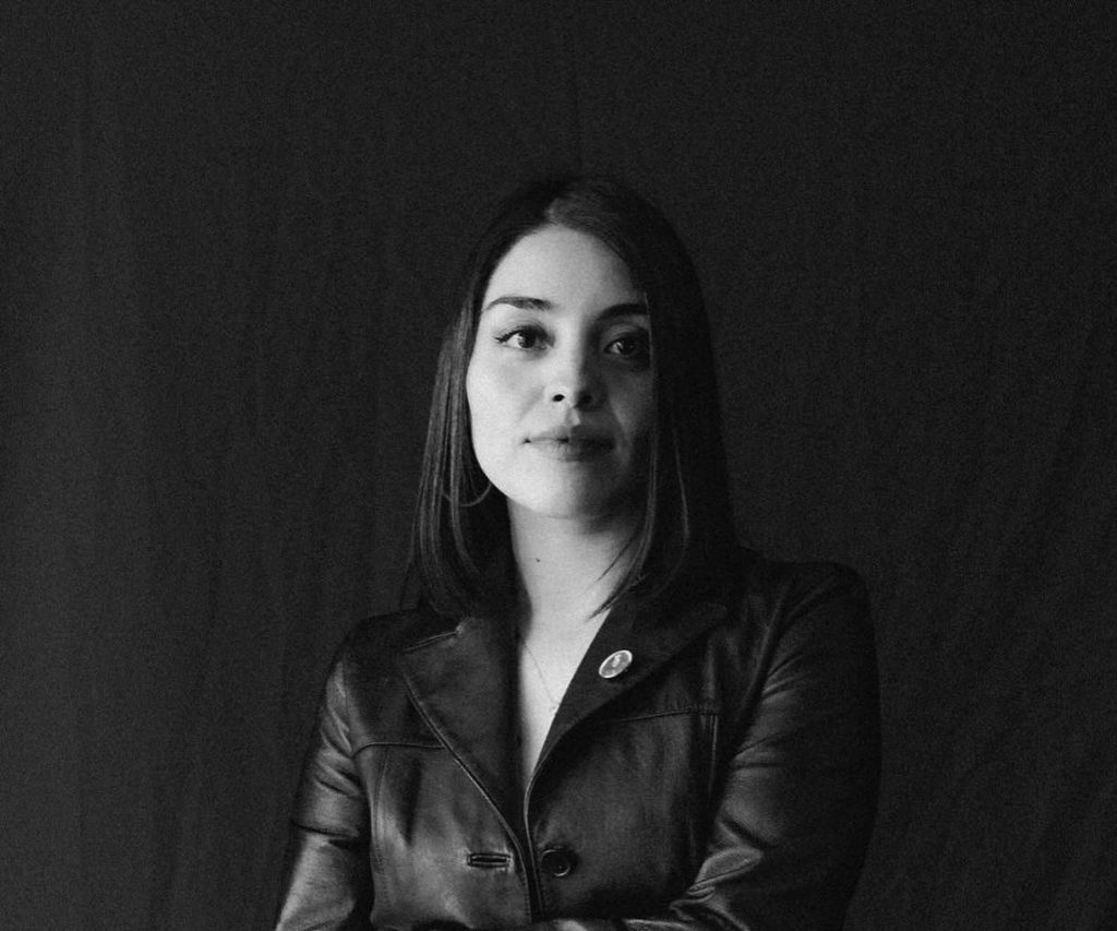 Retrato en blanco y negro de Nina Moure, escritora chilena, mirando hacia arriba con expresión reflexiva contra fondo