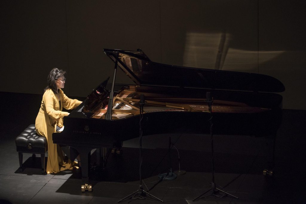 Pianista Liza Chung tocando en escena con piano de cola, iluminada en primer plano durante presentación en Teatro