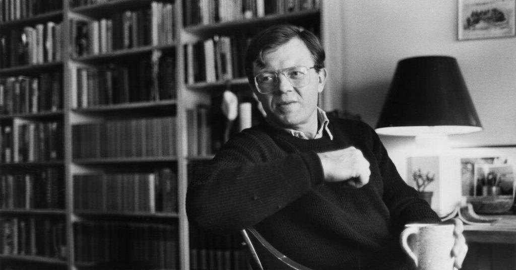 Lance Morrow en su estudio, rodeado de libros, sentado en una silla negra junto a una lámpara
