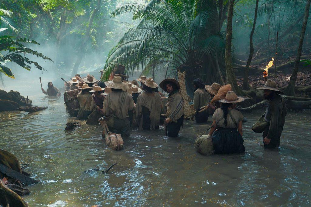 Grupo de actores en río tropical entre vegetación exuberante, escena de drama épico en selva húmeda