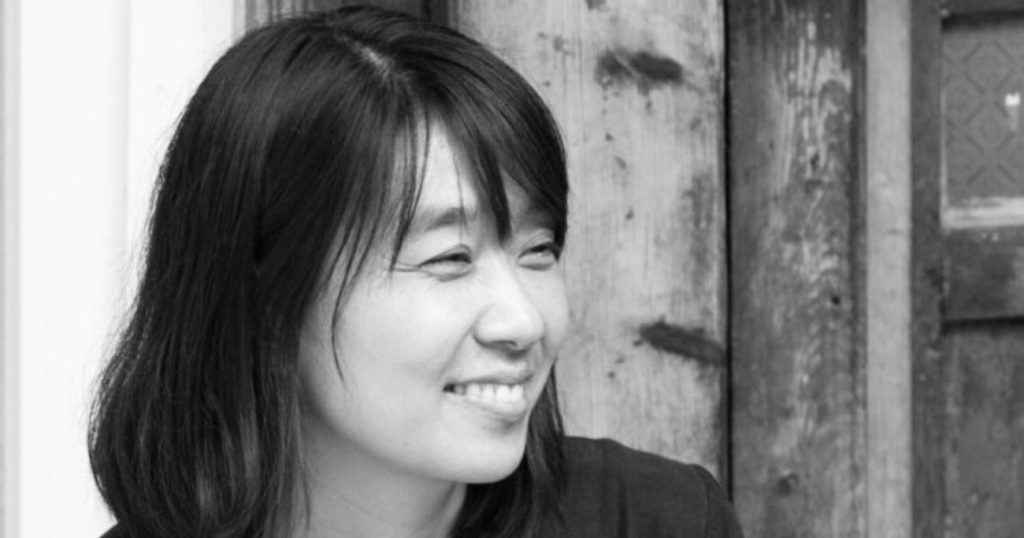 Retrato en blanco y negro de Han Kang, escritora surcoreana, sonriendo de perfil contra fondo de pared desgastada