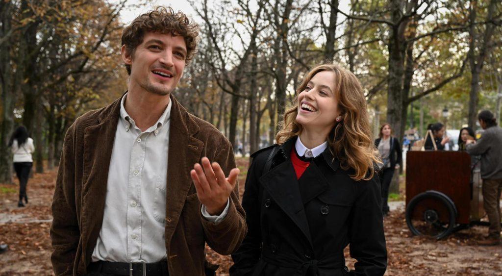 Hombre y mujer caminando por parque otoñal, él gesticulando mientras habla, ella sonriendo, escena de Golpe de suerte