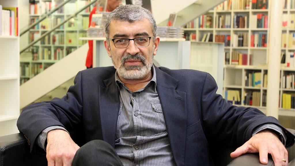 Naief Yehya, escritor y ensayista, sentado en biblioteca con gafas y blazer azul marino
