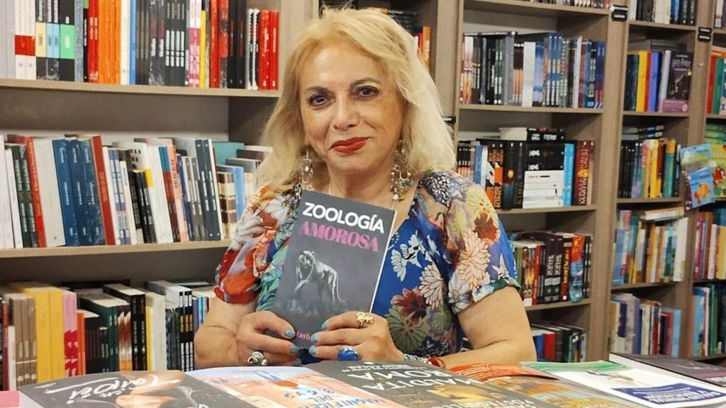 Natasha Valdés sostiene libro frente a estantería con libros, durante presentación literaria