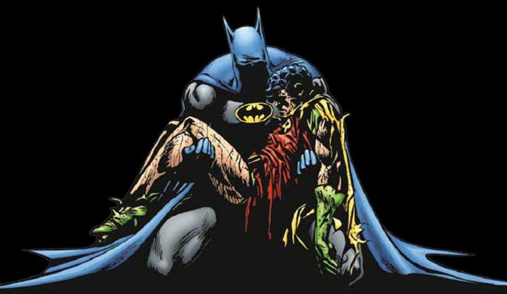 Batman en capa azul y gris sostiene el cuerpo inerte de Robin, rodeado de fuego y destrucción en la noche