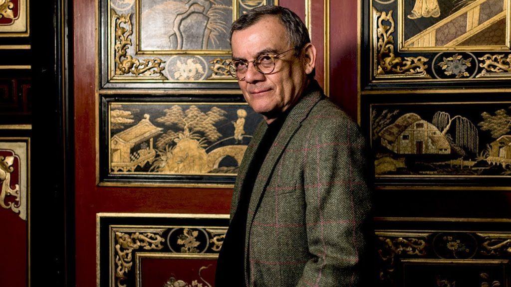 Horacio Castellanos Moya frente a paneles decorativos con motivos orientales dorados y rojos