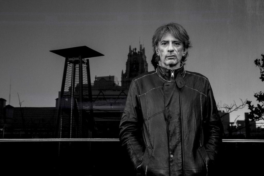 Hombre de mediana edad con chaqueta de cuero oscura ante edificio histórico al atardecer, fotografía en blanco y negro