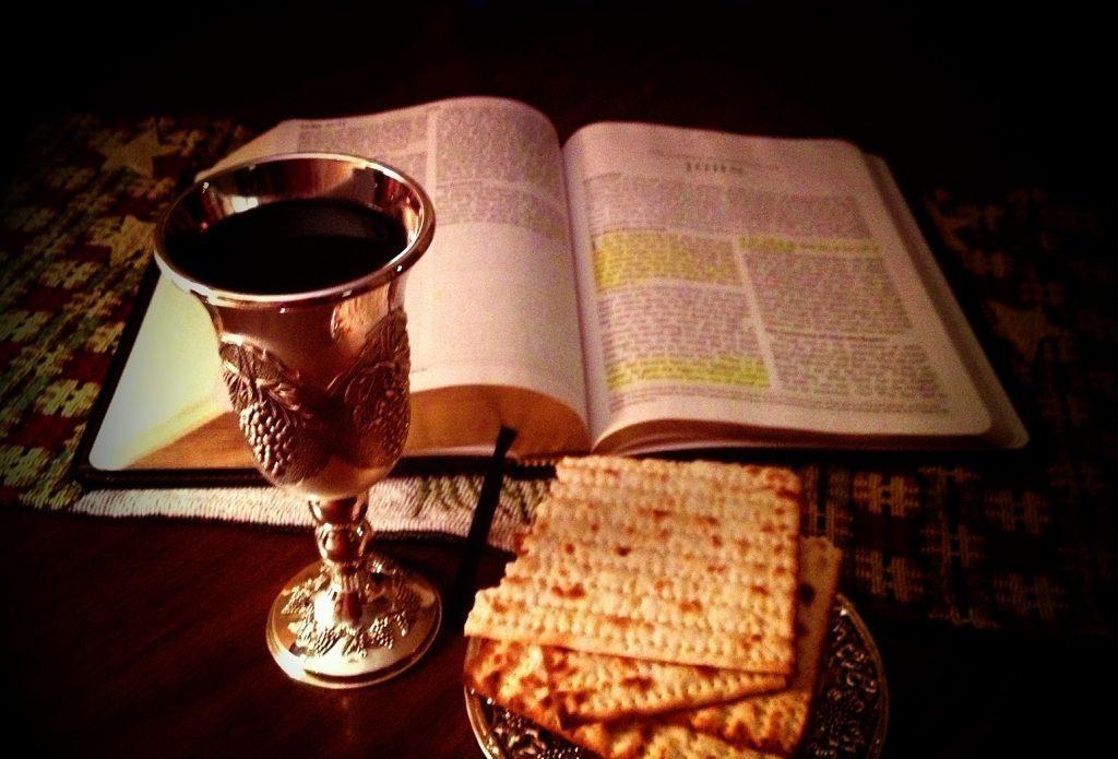 Mesa de Pésaj con biblia abierta, copa de vino sagrada, matzá y velas encendidas sobre mantel decorado