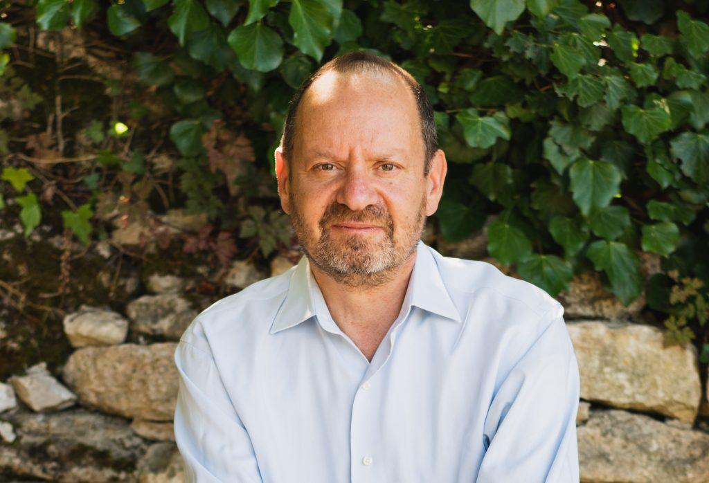 Philippe Sands, abogado y escritor, frente a pared de piedra con hiedra verde, vistiendo camisa azul claro