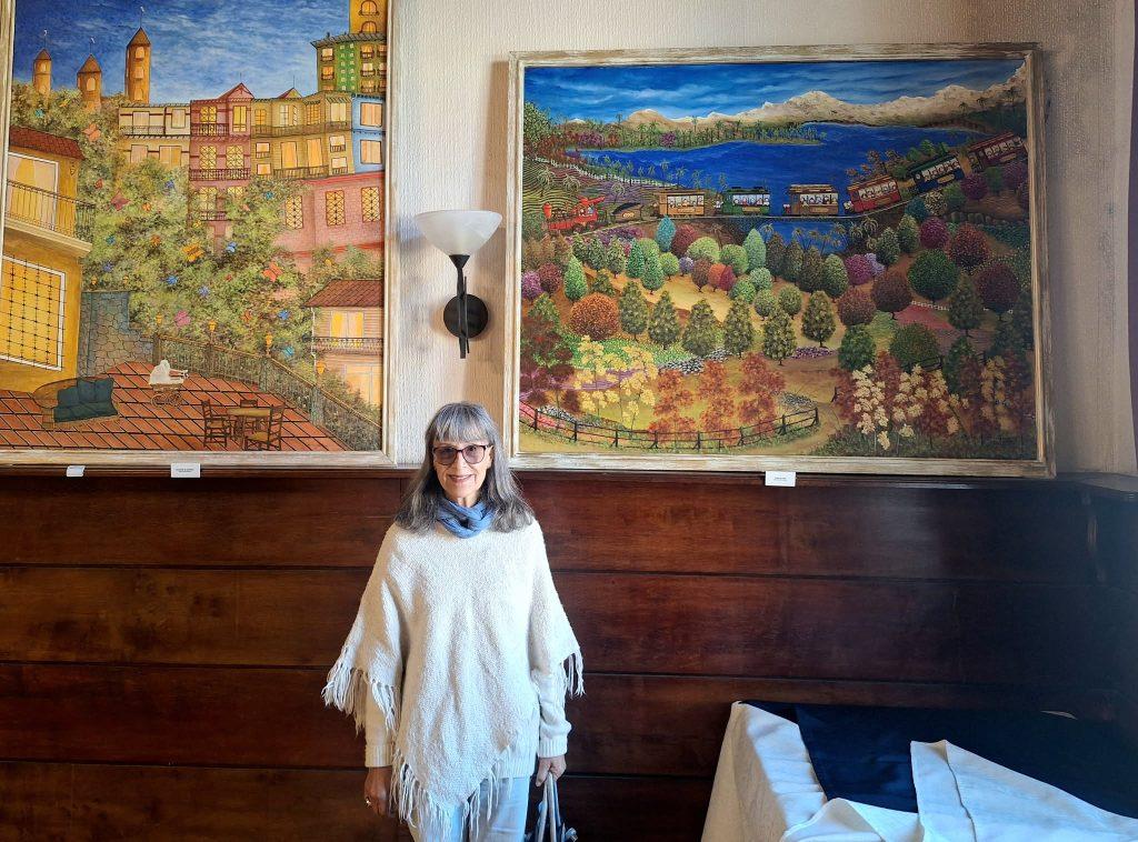 Mujer frente a dos cuadros de paisajes coloridos en interior con paneles de madera oscura