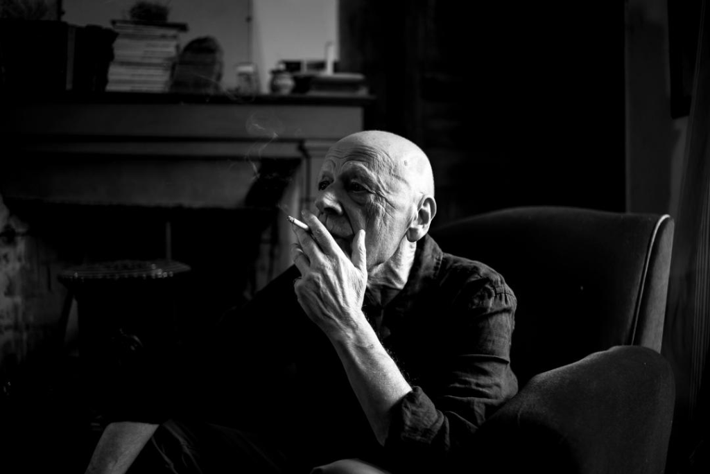 Pierre Michon, escritor francés, en blanco y negro apoyando su cabeza en la mano mientras trabaja frente