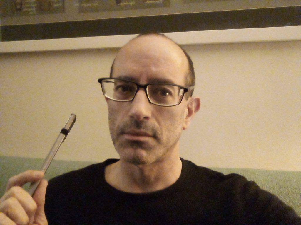 Nicolás Poblete, hombre de mediana edad con gafas y bigote, sostiene un bolígrafo en primer plano