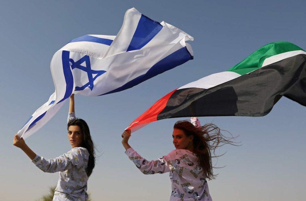 Dos mujeres sostienen banderas de Israel y Palestina bajo el cielo despejado, simbolizando la coexistencia y el diálogo