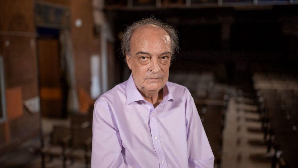 Enrique Vila-Matas, escritor español, en primer plano con camisa lavanda en interior de arquitectura moderna