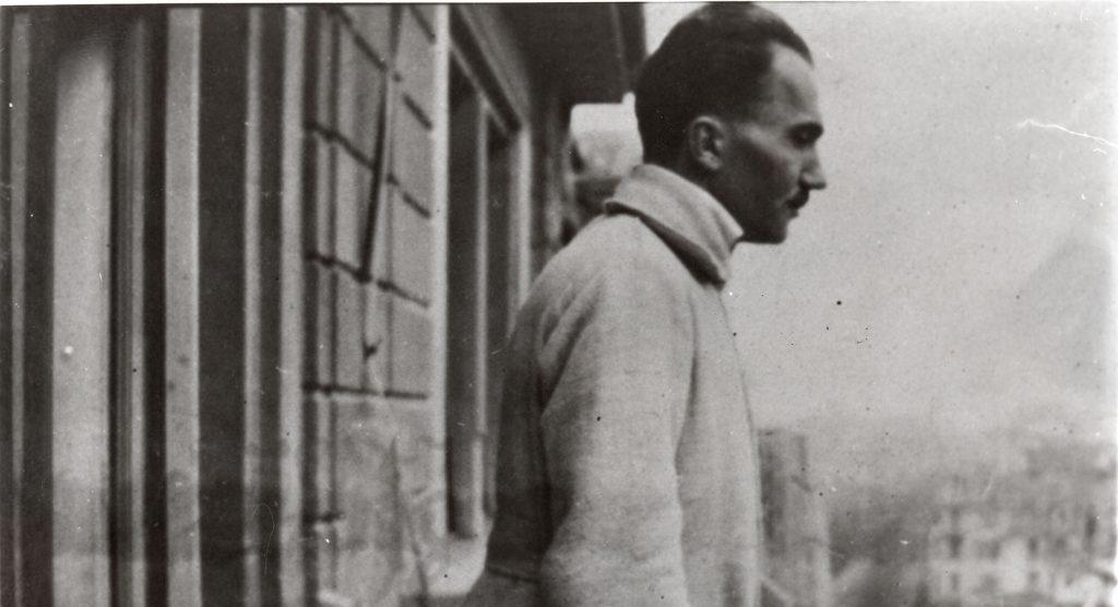 Nikos Kazantzakis de perfil junto a una ventana con vistas urbanas de fondo