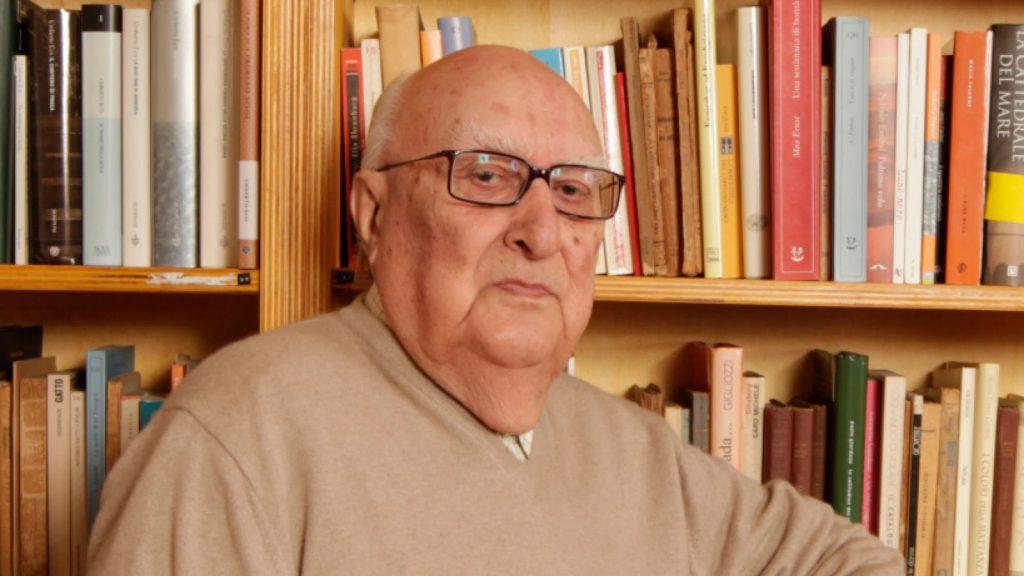 Hombre mayor con gafas frente a una estantería de libros, autor de novela negra italiana