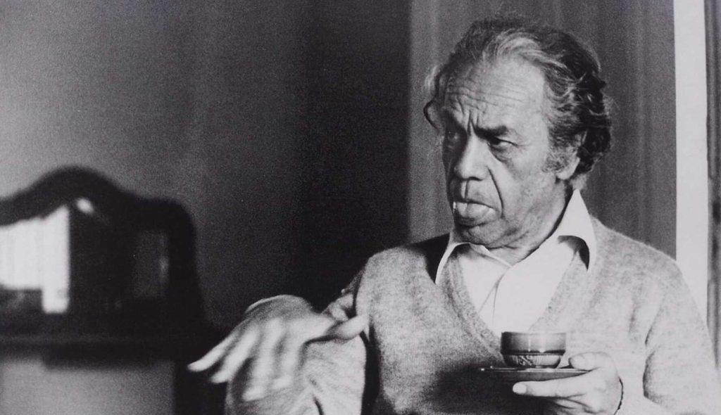 Nicanor Parra sostiene una taza de café en blanco y negro, mirando hacia un lado en ambiente interior