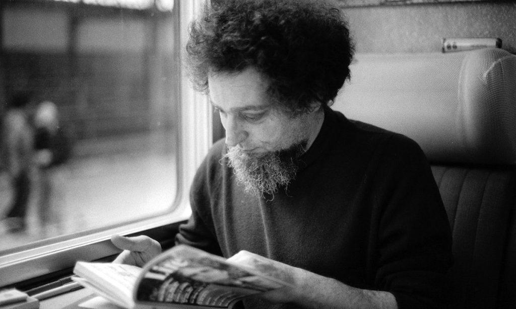 Georges Perec leyendo un periódico junto a una ventana, fotografía en blanco y negro de los años 60