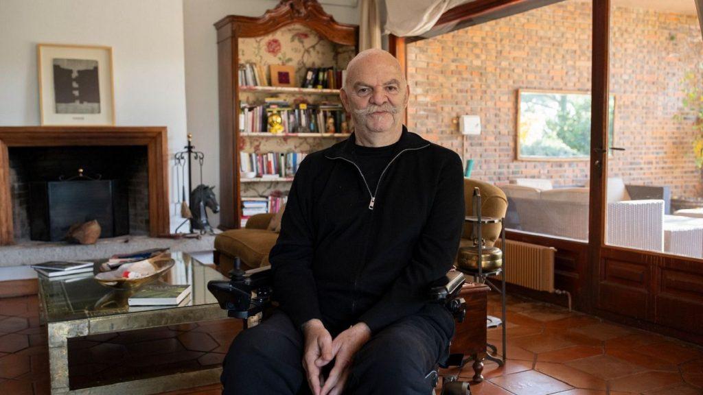 Escritor Martín Caparrós sentado en sillón de madera dentro de estudio con libros y chimenea al fondo