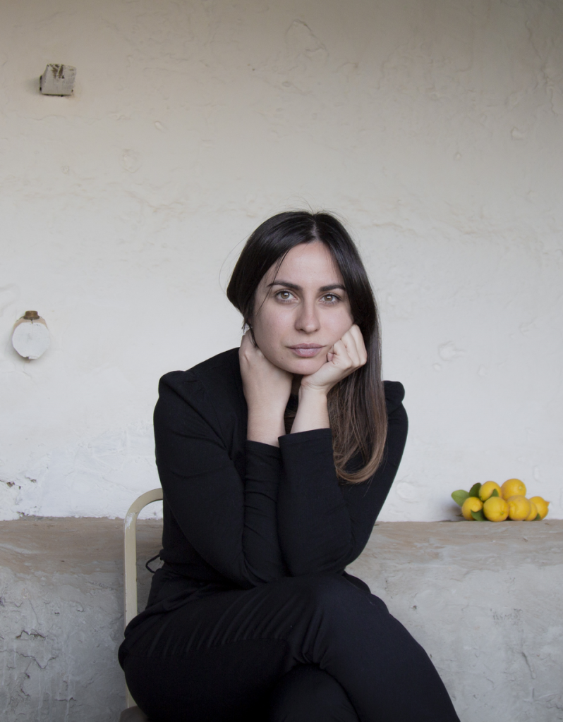 María Sánchez Rodríguez apoya su cabeza en la mano, vistiendo blazer negro, sentada frente a pared blanca con limones