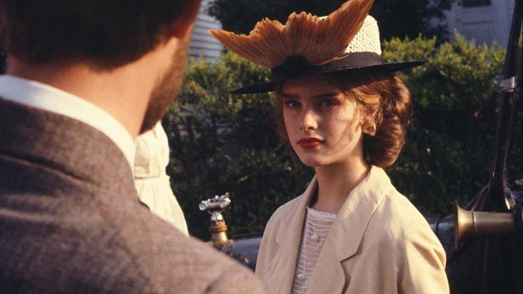 Mujer joven con sombrero de vaquero conversando con un hombre en escena de Pretty Baby, ambiente exterior con vegetación