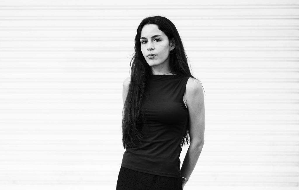 Adriana Murad, mujer de cabello largo oscuro, viste blusa negra sin mangas contra fondo blanco