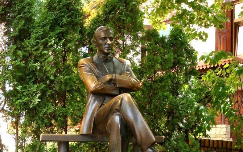 Estatua de bronce de Mijaíl Bulgákov sentado con los brazos cruzados, rodeado de hiedra verde en un patio
