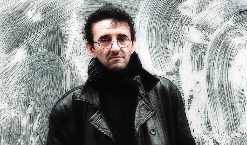 Roberto Bolaño, escritor chileno, retrato frontal con expresión seria frente a fondo abstracto gris