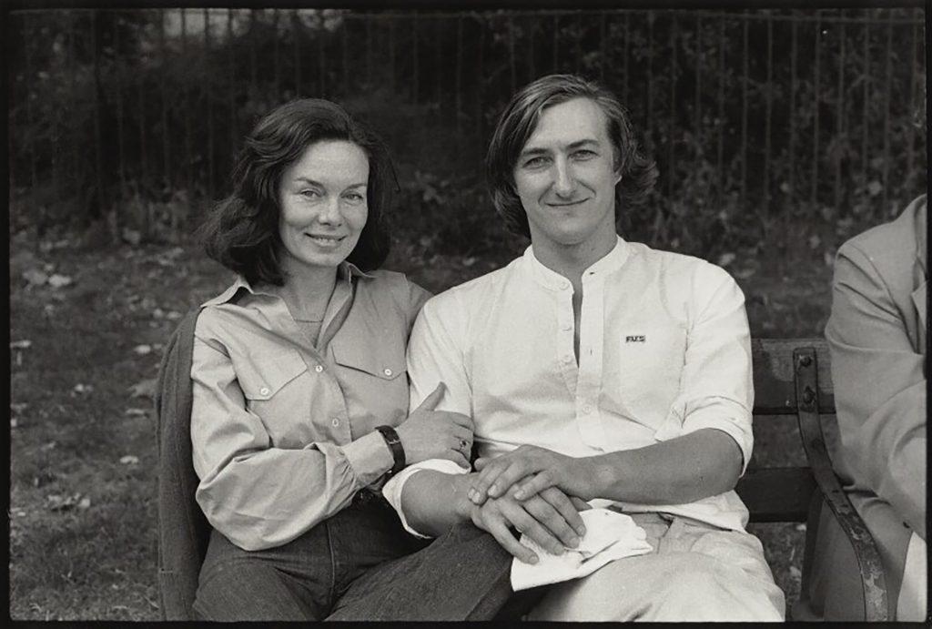 Fotografía en blanco y negro del escritor británico Julian Barnes, joven, sentado en un banco al aire libre junto a una mujer