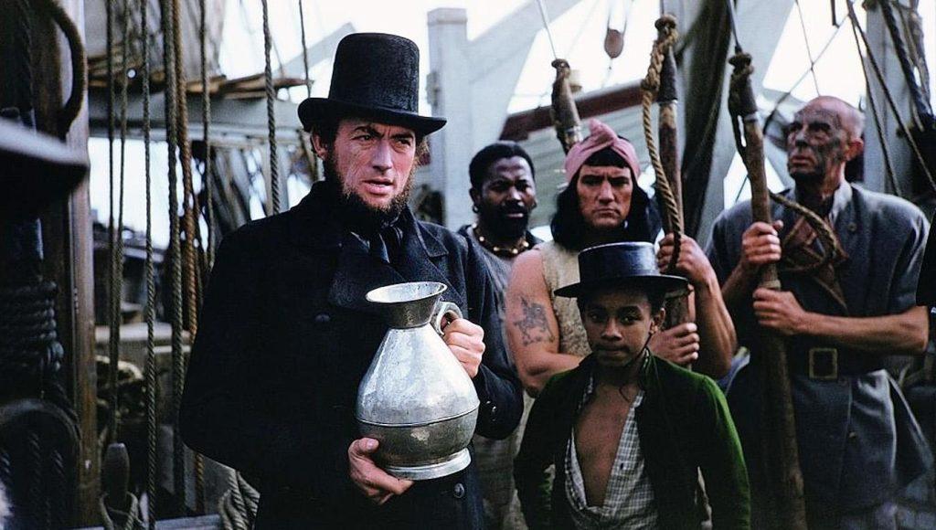 Fotograma de la película «Moby Dick»: el capitán Ahab, con sombrero de copa, sostiene una jarra a bordo del ballenero rodeado por su tripulación